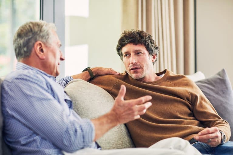 Younger man talks to an older man while sitting on a couch